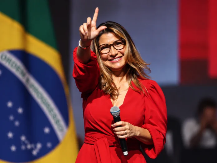 Janja Lula da Silva durante evento político com bandeira do Brasil ao fundo